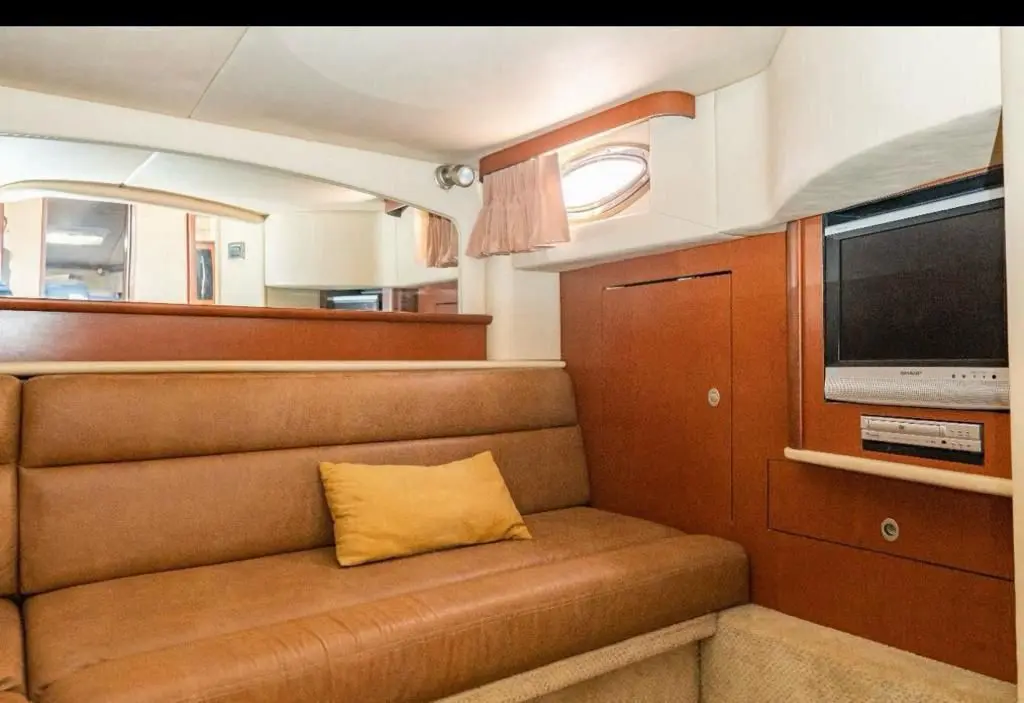 Yacht cabin with a tan leather sofa, porthole and flat-screen TV set in wood cabinetry