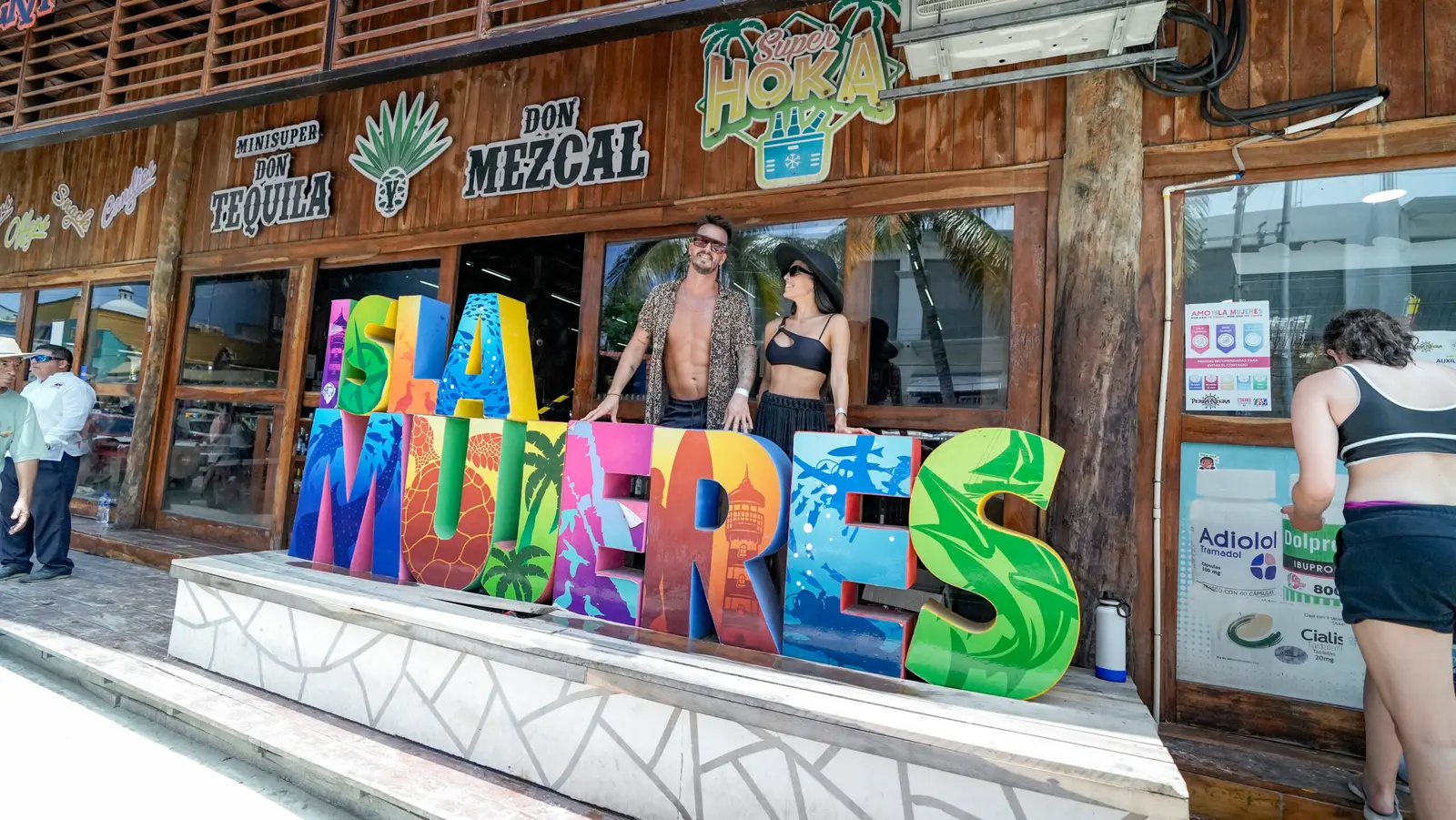 Couple posing behind the colorful Isla Mujeres letter sign in front of a tequila shop