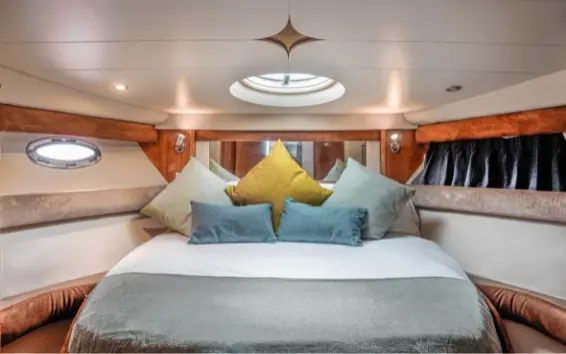 Below-deck cabin of the yacht with a double bed, cushions and porthole windows