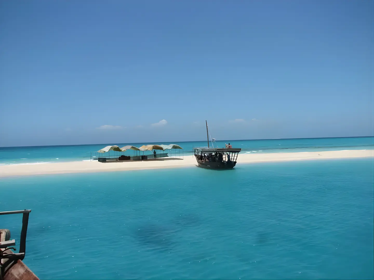 Wooden dhow moored off Nakupenda Sandbank's white sand, sun shades set up on the beach