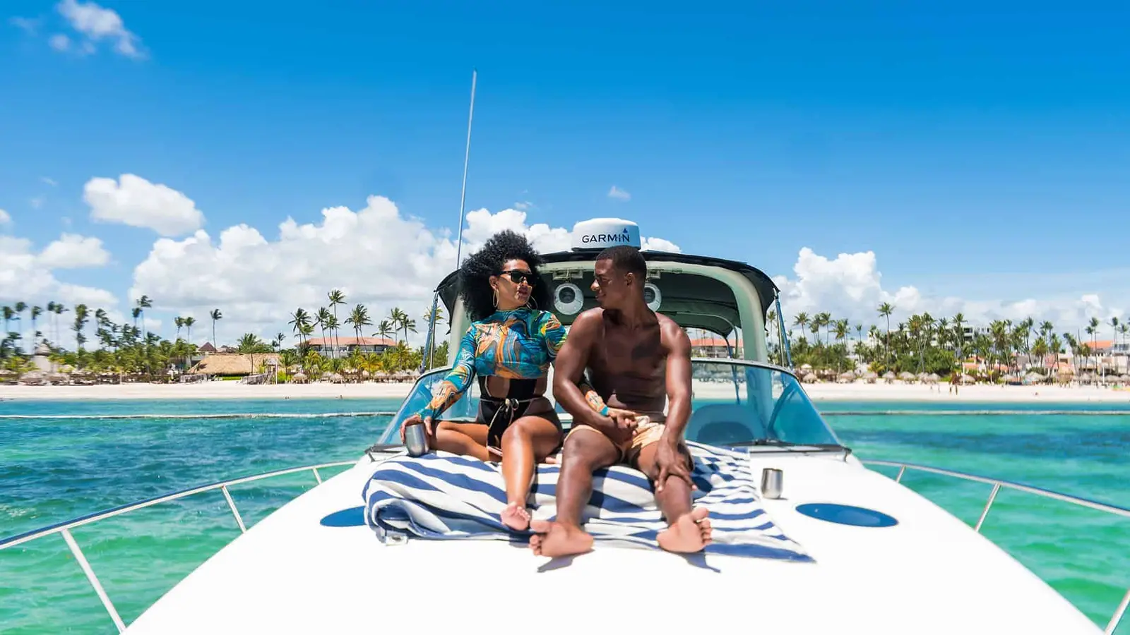 Couple relaxing on a striped towel on the yacht's bow with Bávaro Beach behind