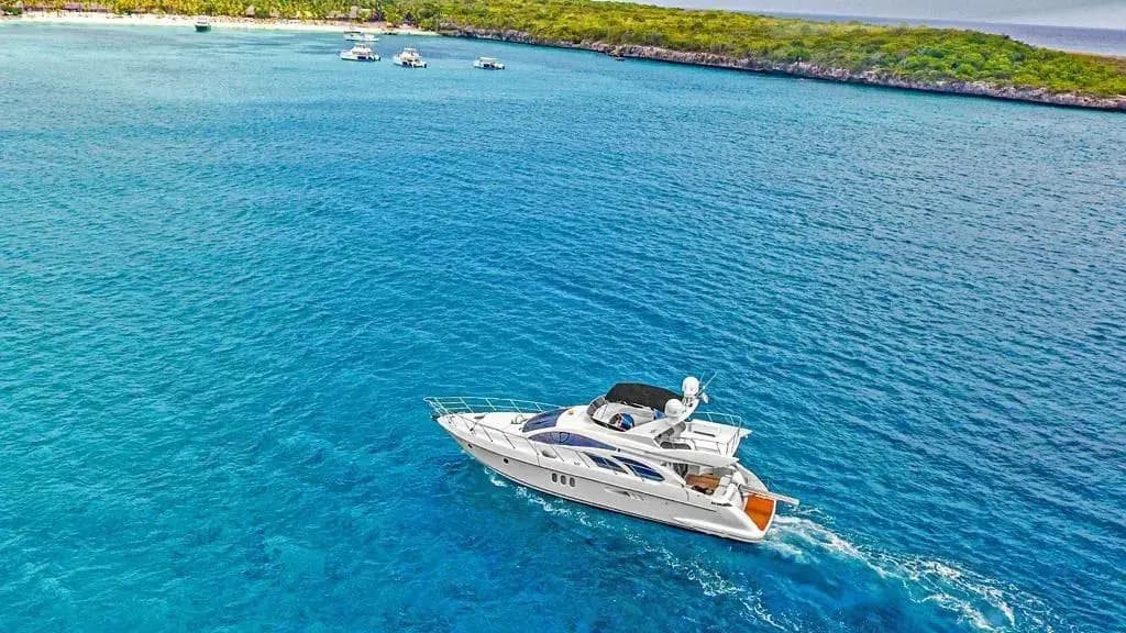 Saona Island Weather aerial view of a luxury yacht cruising across crystal clear turquoise waters near the lush tropical coastline of Saona Island on a bright, sunny day.