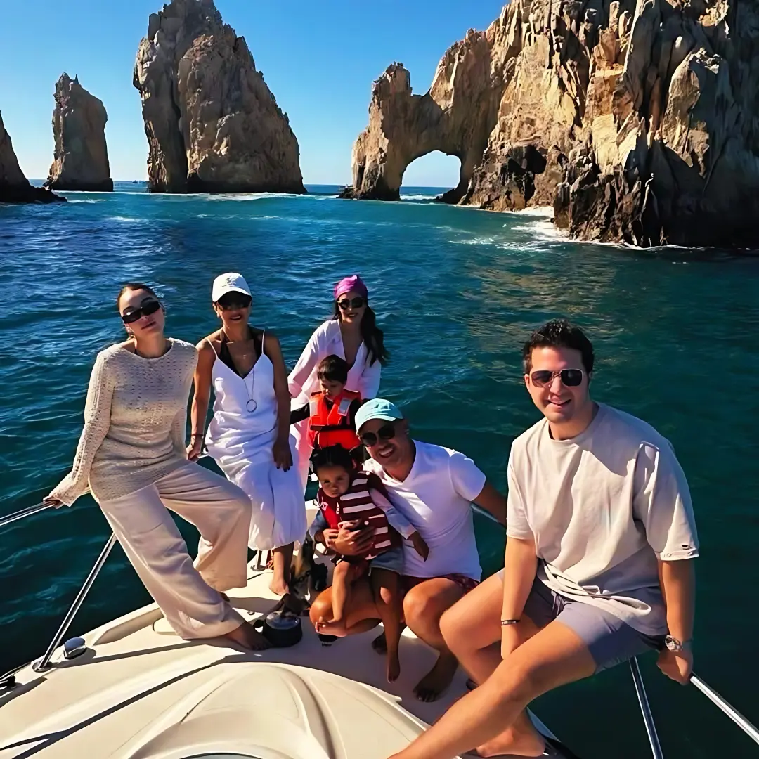 Family with two kids sitting together on a yacht's bow in front of El Arco
