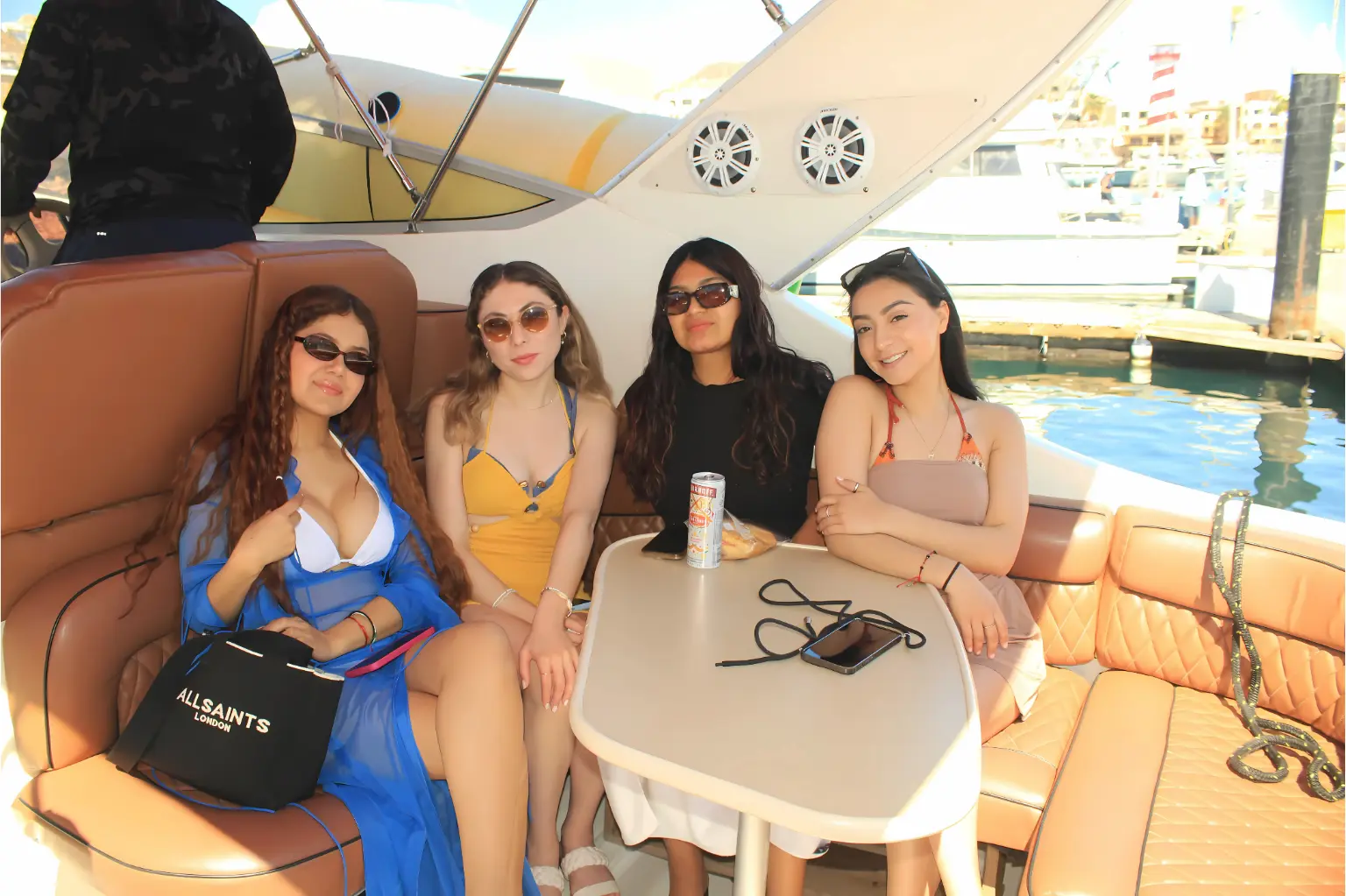 Four women in sunglasses seated around the cockpit table of a yacht docked in the Cabo San Lucas marina
