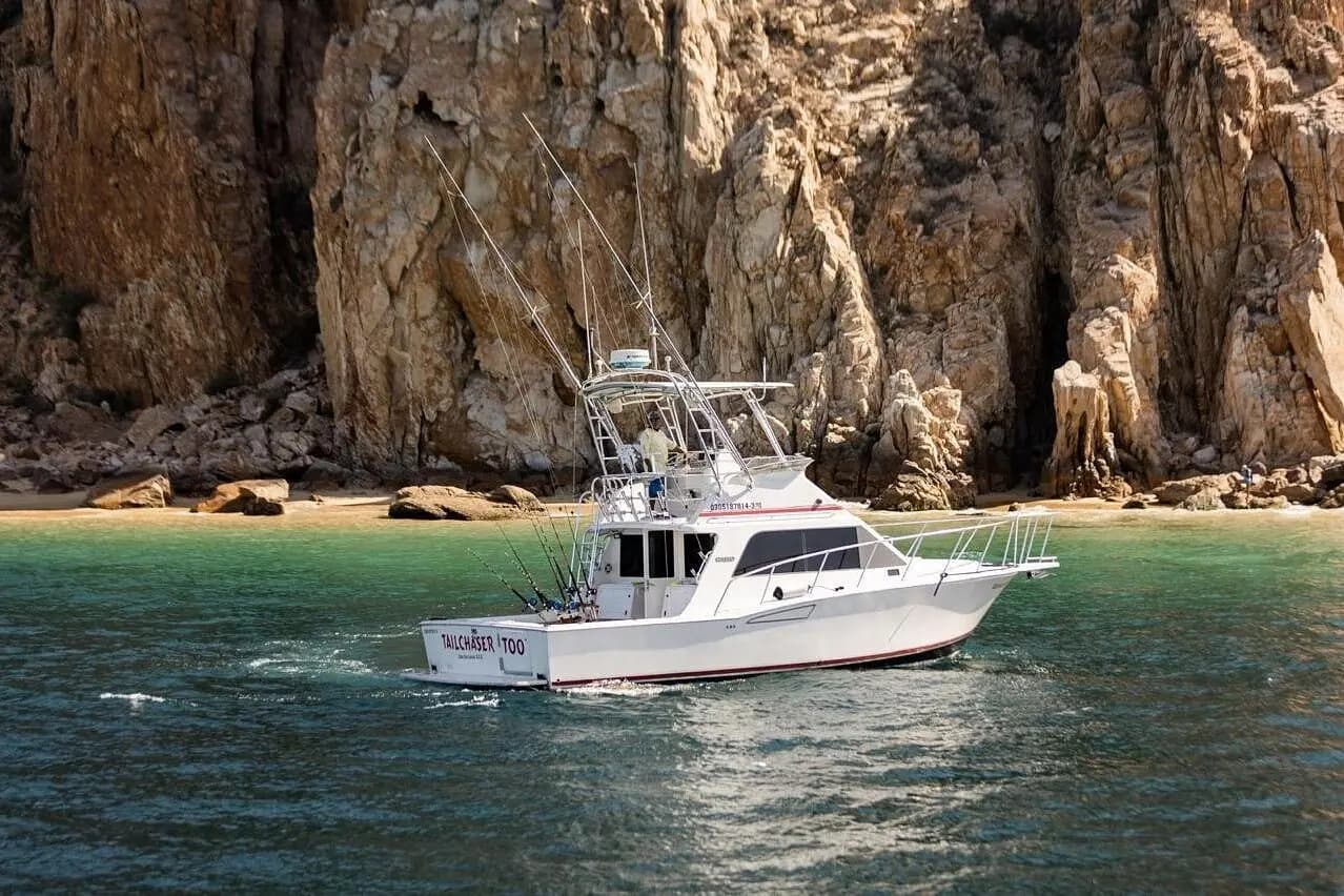 Flybridge sportfishing yacht anchored in green water beneath tall granite cliffs in Los Cabos