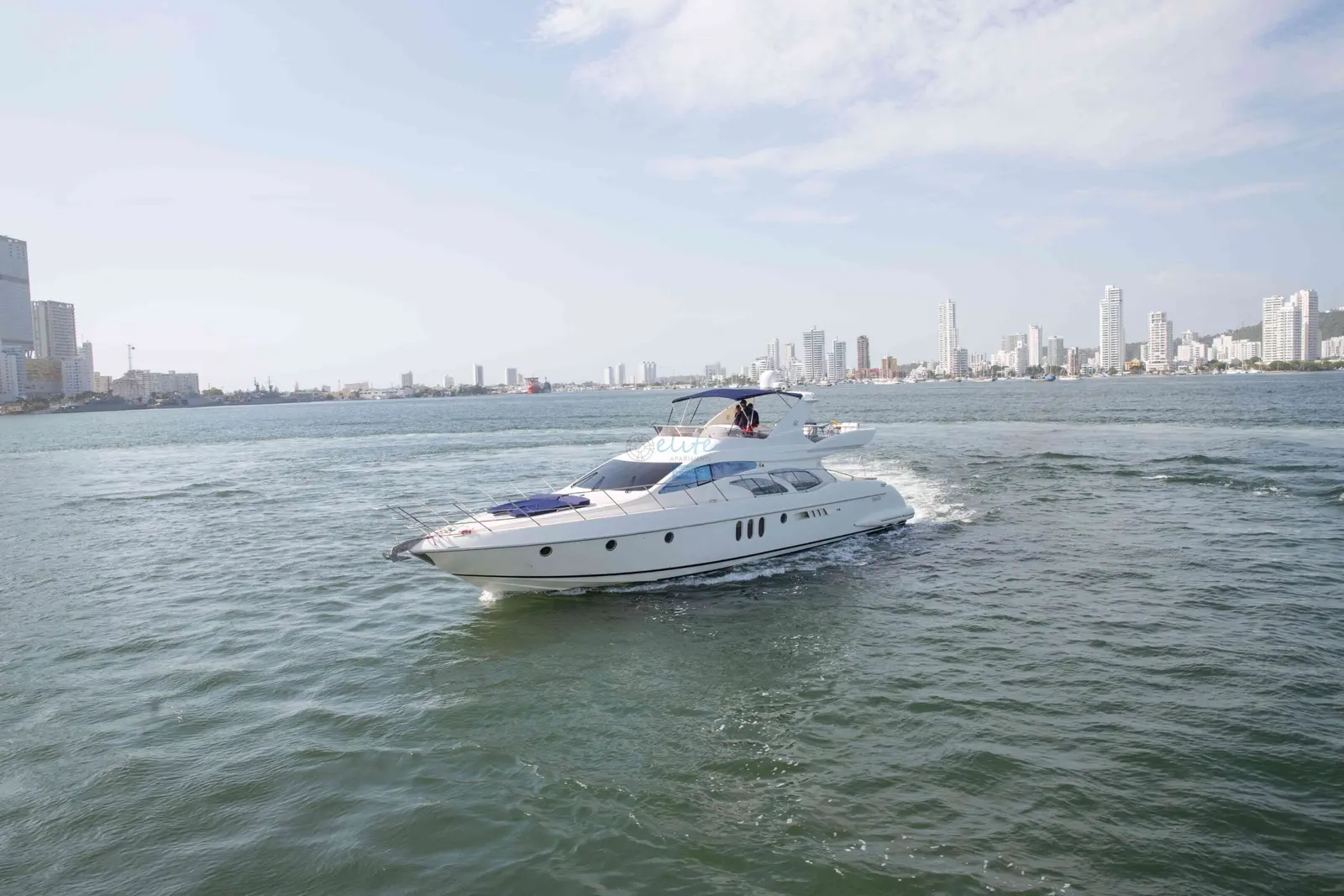 White flybridge motor yacht cruising across the bay with Cartagena's high-rise skyline behind