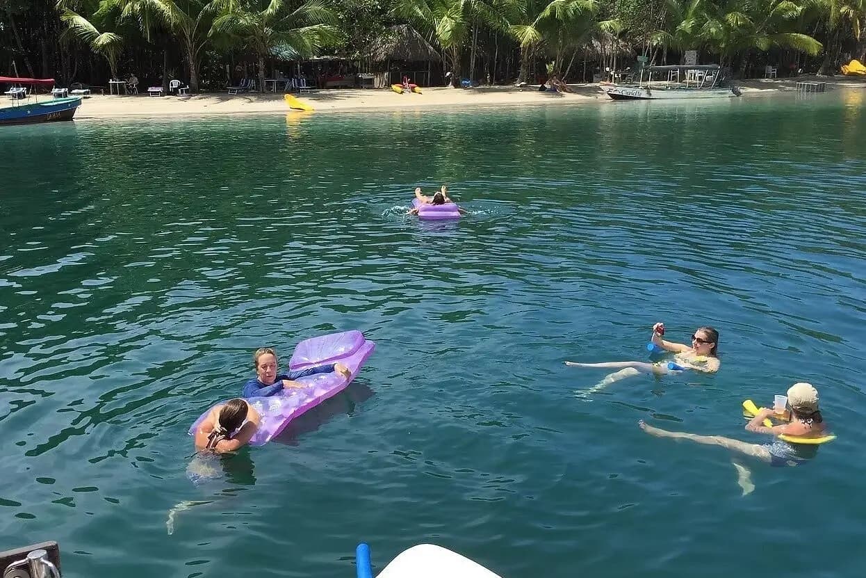Guests swimming and floating on purple inflatables in a calm bay off a palm-fringed Bocas del Toro beach