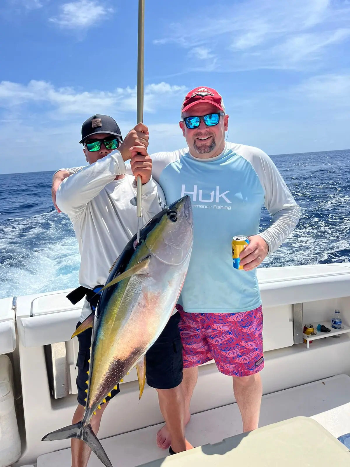Two men hold up a yellowfin tuna on the stern of the sportfishing yacht, one with a beer in hand
