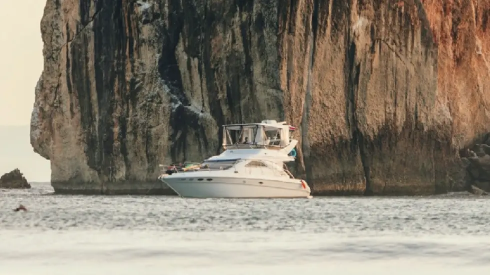 Motor yacht anchored below a towering rock face beside a pale sand beach in Papagayo