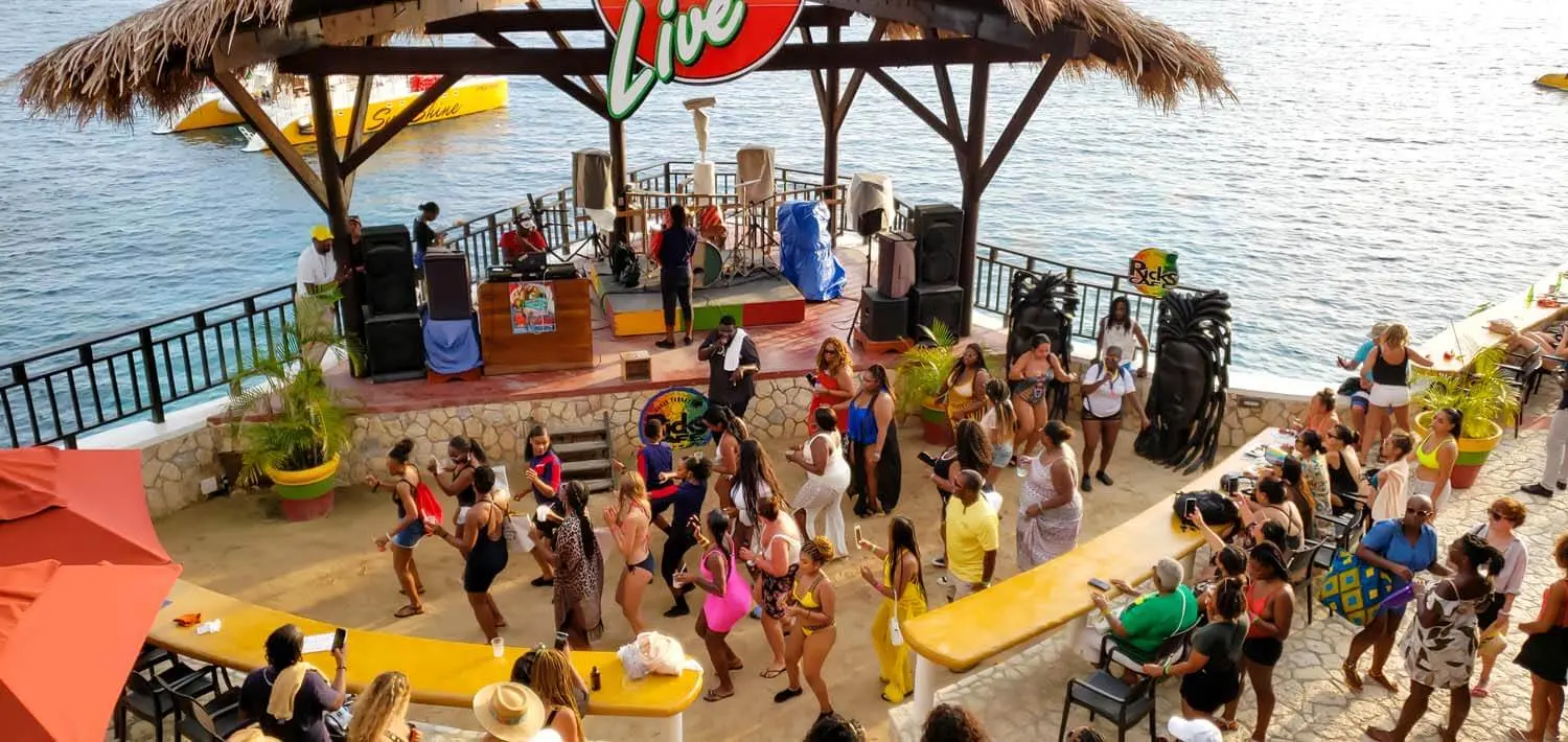 Crowd dancing on a seaside terrace in front of a thatched music stage in Negril