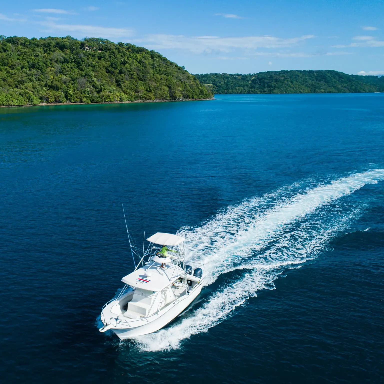 Sportfishing boat speeding across deep blue water past green hills on the Guanacaste coast