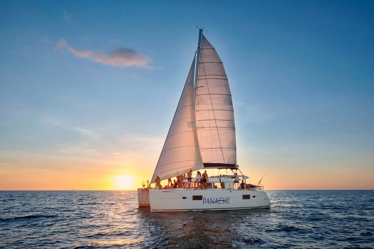Sailing catamaran under full sail with guests on deck as the sun sets over the sea off Costa Rica