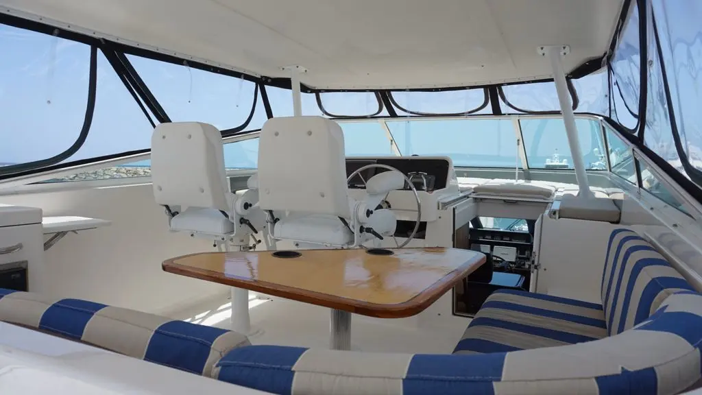 Enclosed flybridge of the motor yacht with twin helm chairs, a wooden table and striped seating