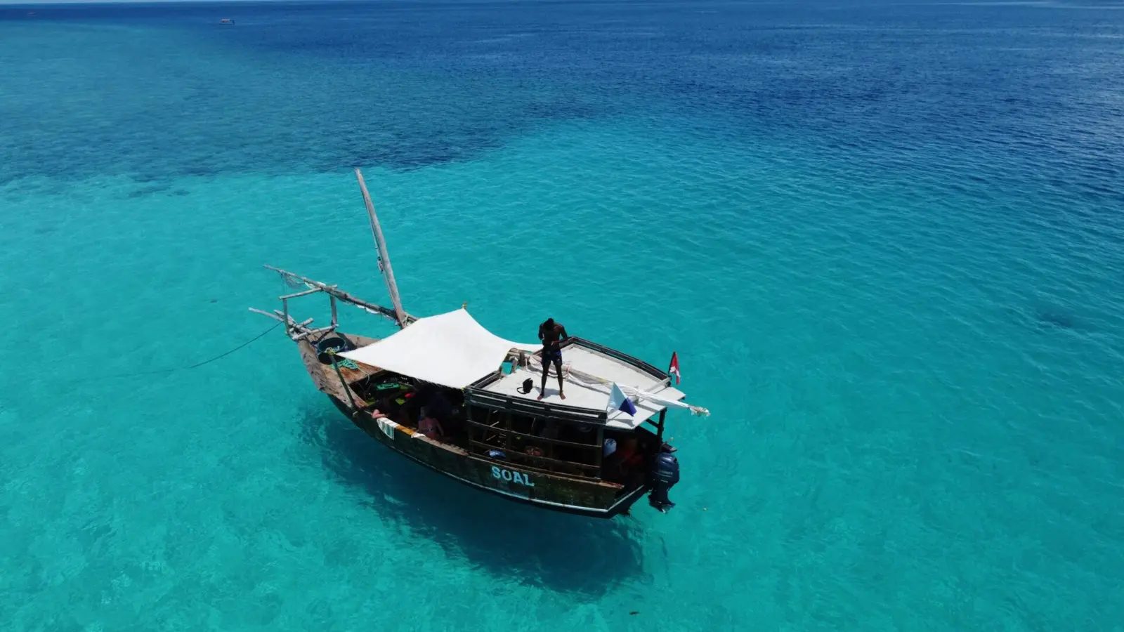 Aerial view of a wooden dhow with a white sun canopy anchored in turquoise water off Zanzibar