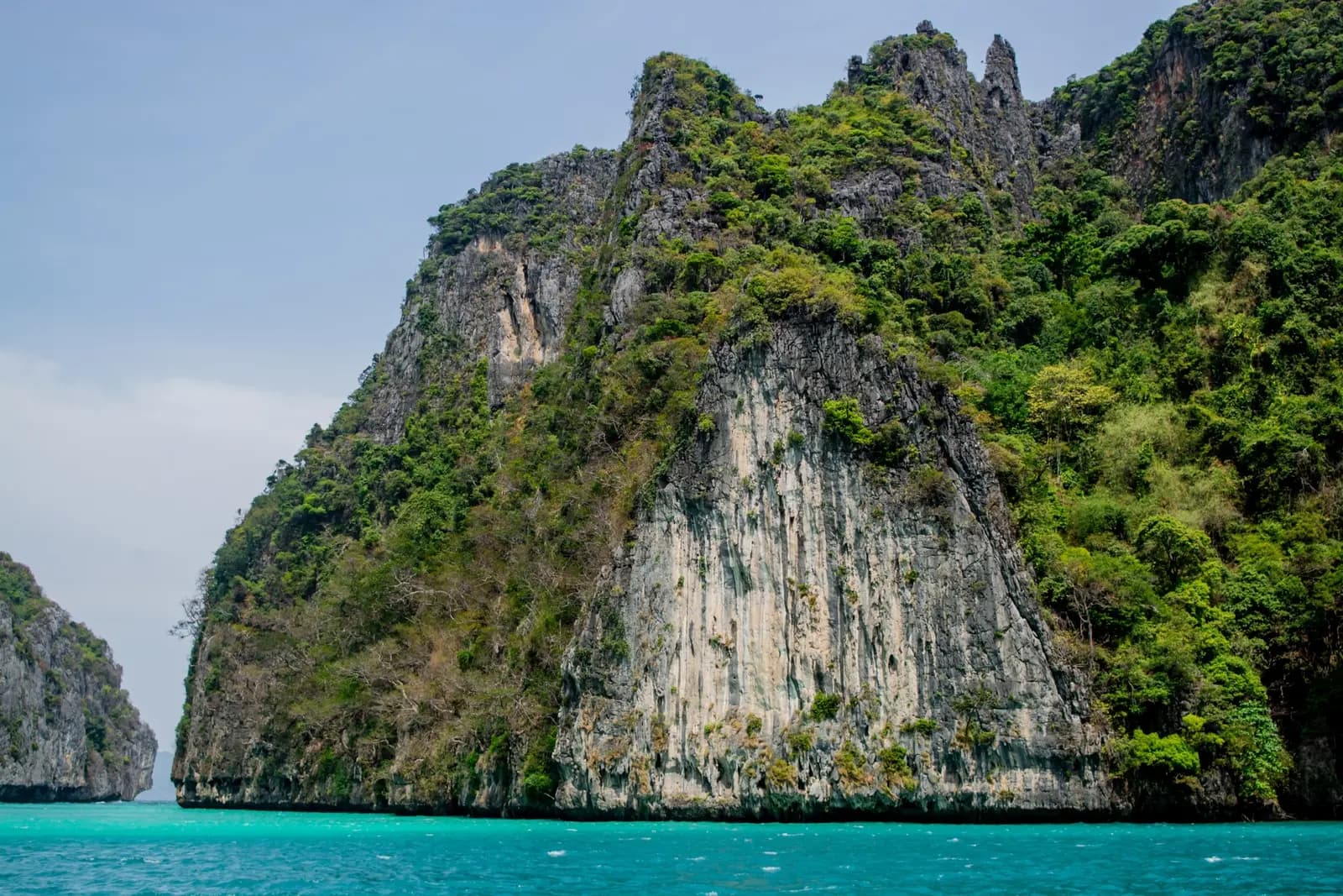 Sheer limestone cliffs draped in jungle towering over turquoise water in the Phi Phi Islands