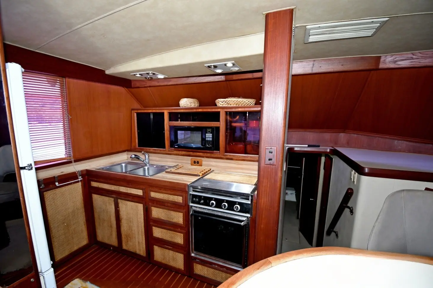 Wood-paneled galley with a steel sink, stove and microwave inside a sportfishing boat