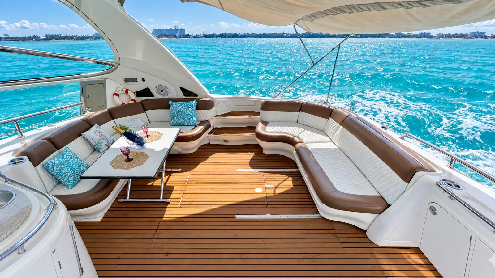 Shaded aft cockpit of a motor yacht with U-shaped seating as a white wake trails over turquoise water