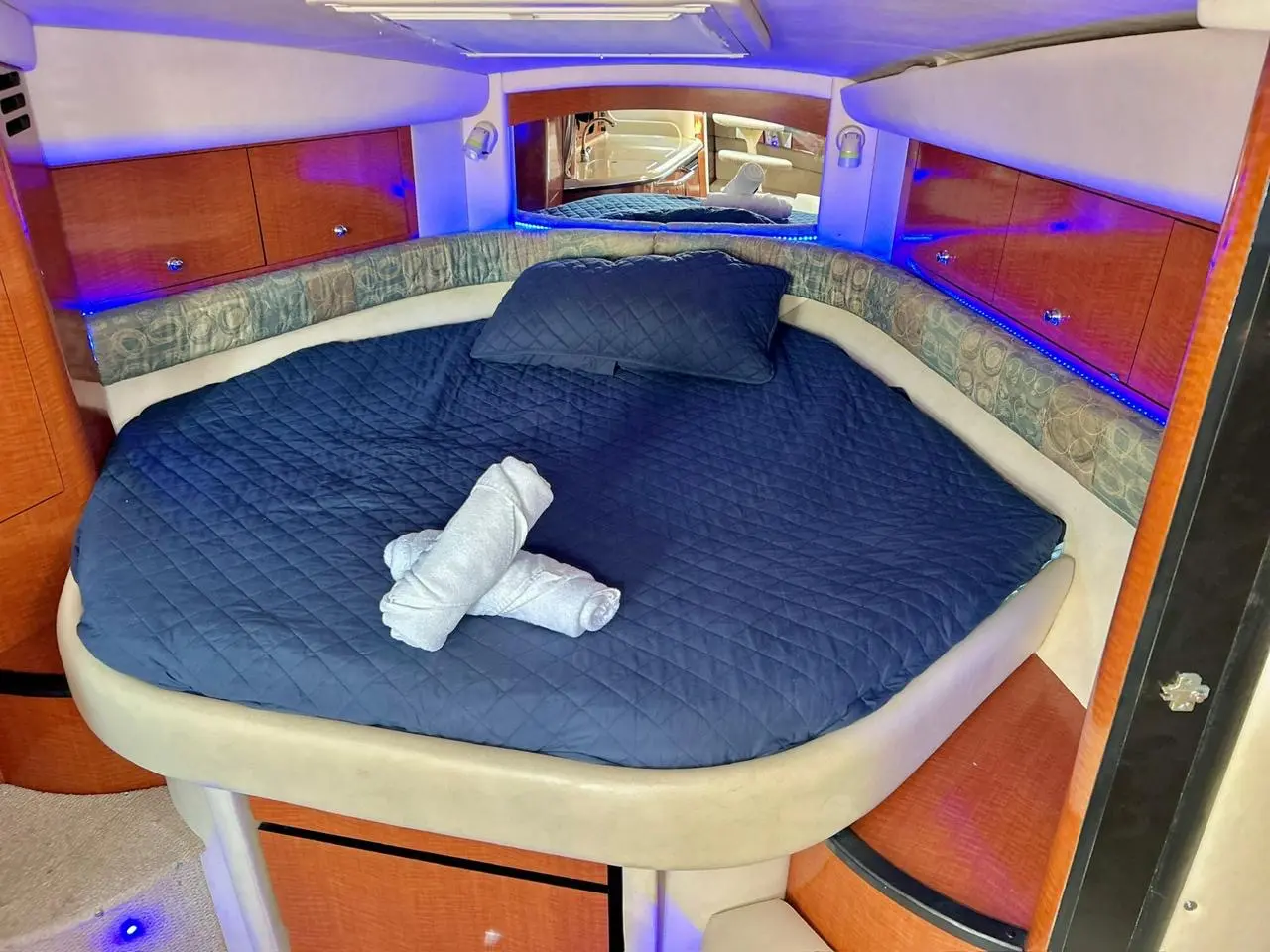 Forward berth with a navy quilted cover, rolled towels and blue accent lighting in a yacht cabin
