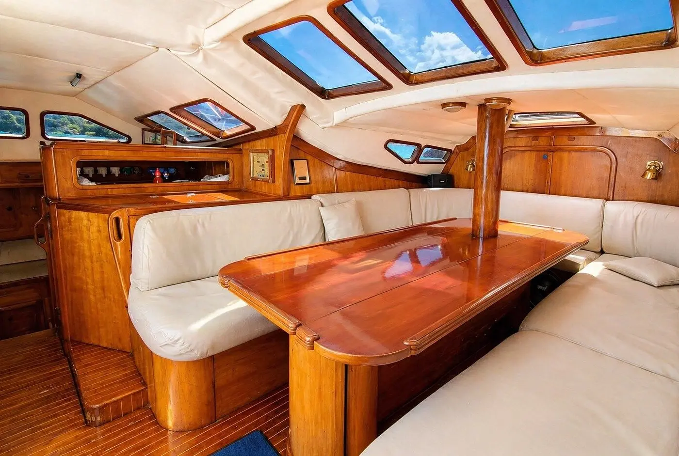 Angled view of a wood-trimmed saloon with a glossy table, cream cushions and a row of skylight hatches