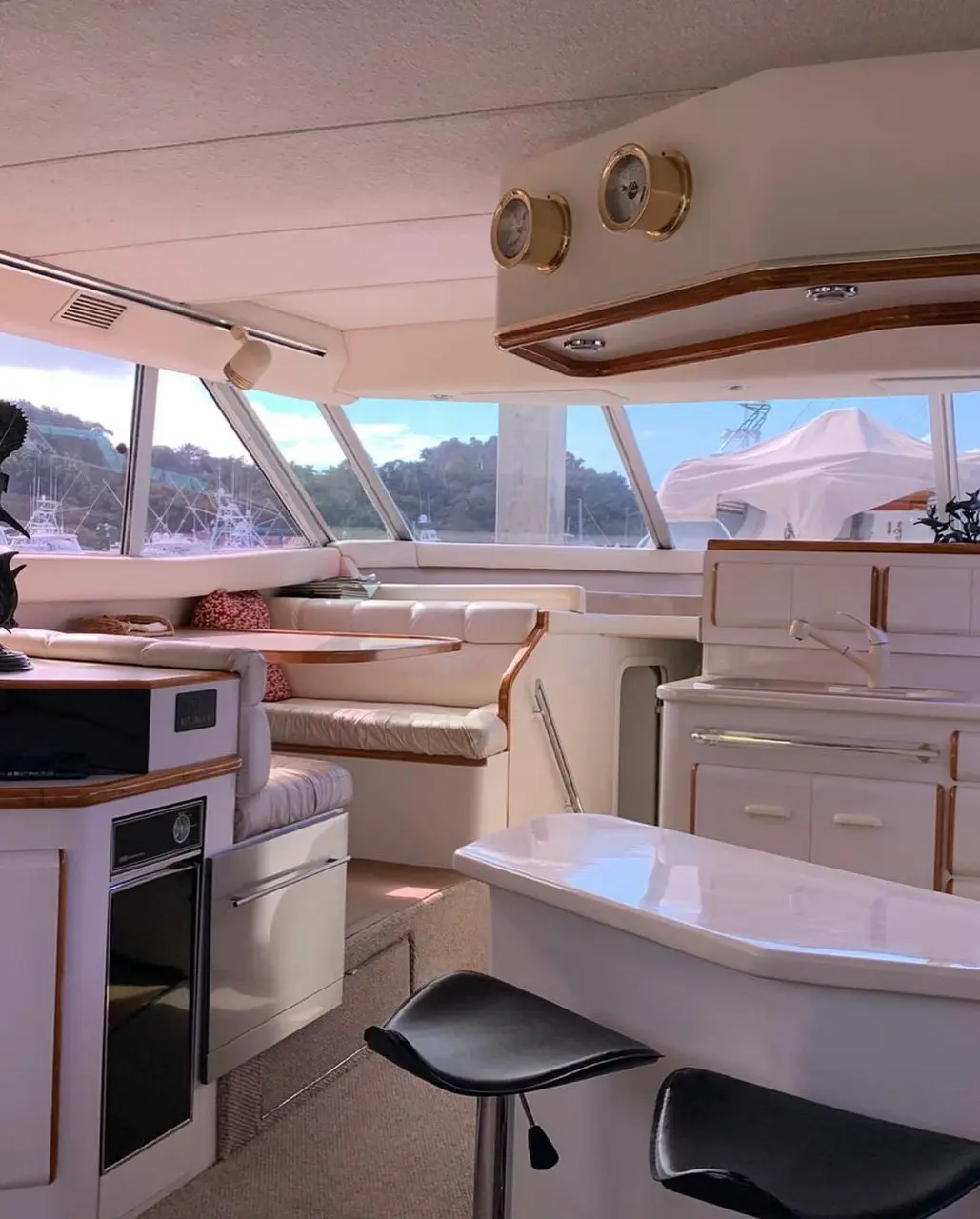 Motor yacht galley with white cabinets, an oven and bar stools at the counter, windows framing green hills