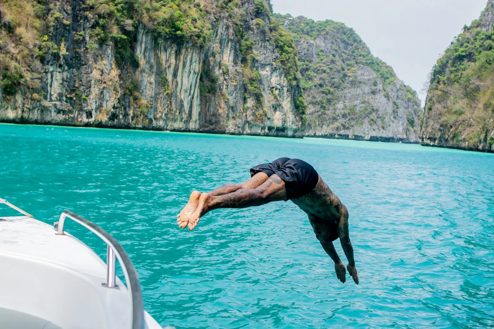 Man diving headfirst off a speedboat into a turquoise lagoon ringed by limestone cliffs at Phi Phi