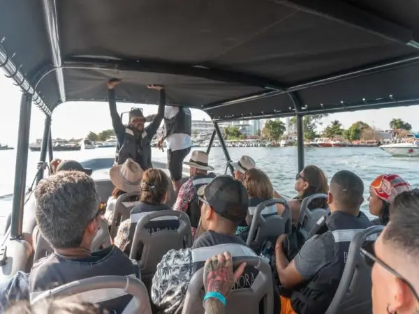 Packed speedboat of guests in life jackets listening to the standing guide, open water and coast behind
