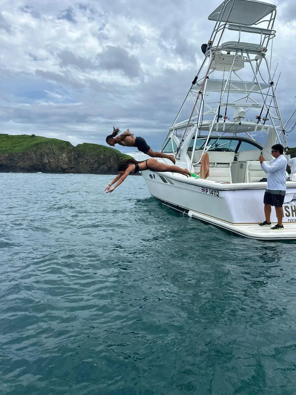 Two men leap off the side of the anchored sportfishing yacht into a calm Costa Rica bay