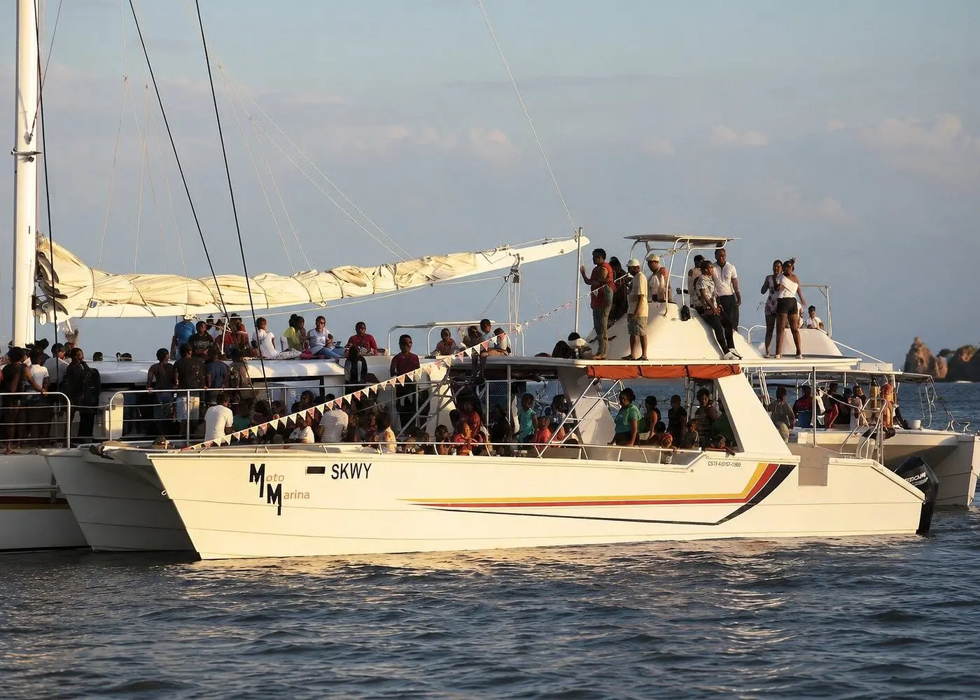 Whale watchers crowding the decks of catamarans lined up side by side in golden light on Samaná Bay