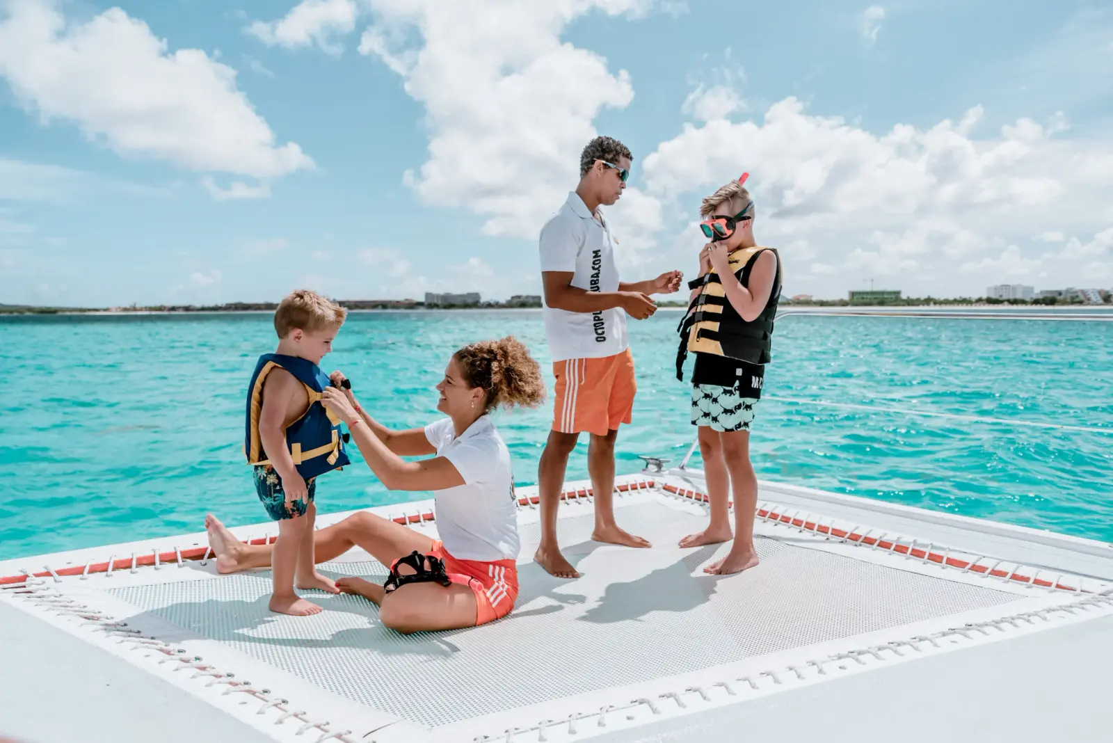 Crew members fitting two kids with life vests and snorkel masks on the catamaran net off Aruba