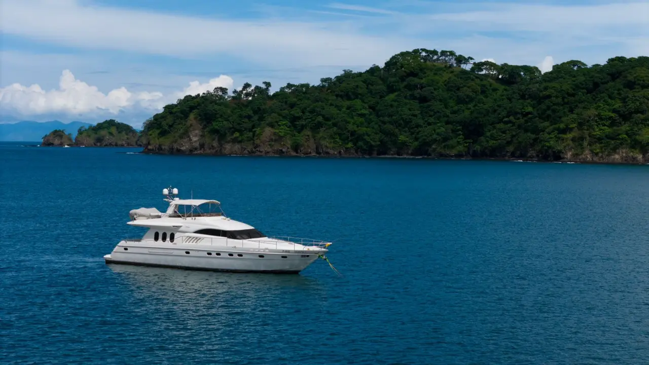 Flybridge motor yacht anchored in a calm blue bay beneath a forested headland in Papagayo