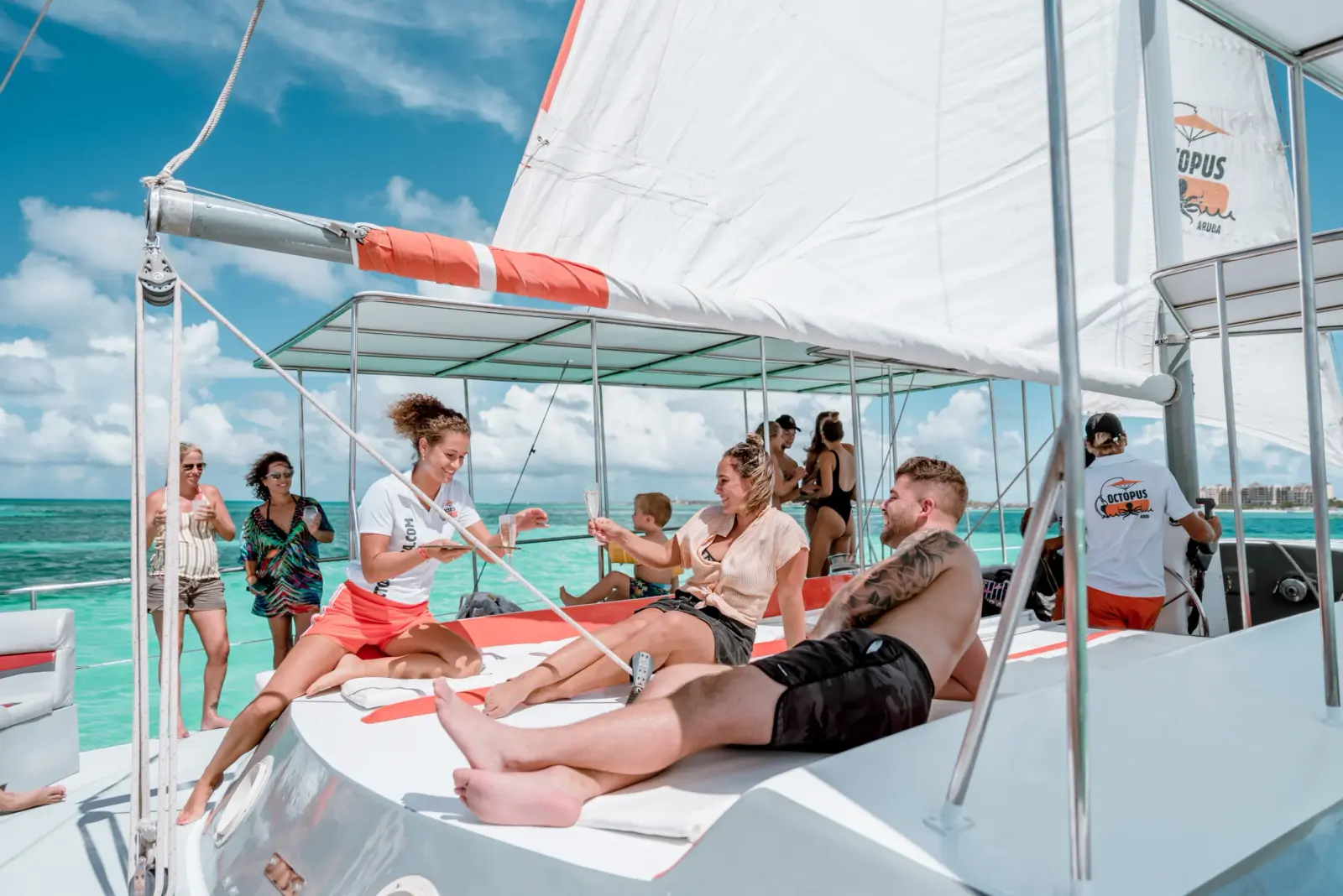Guests relaxing on the front deck of a sailing catamaran under its white sail off Aruba