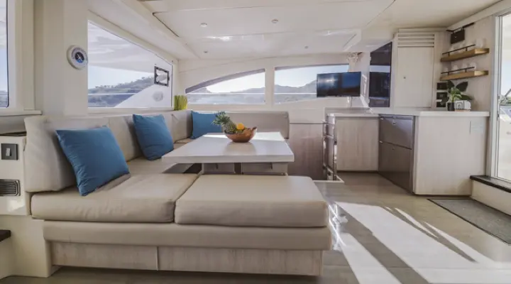 Power catamaran salon with a wide cream lounge, blue cushions and a sunlit galley