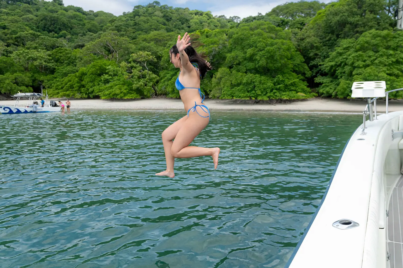 A woman jumps off the side of the fishing boat into calm water off a jungle-backed beach in Costa Rica
