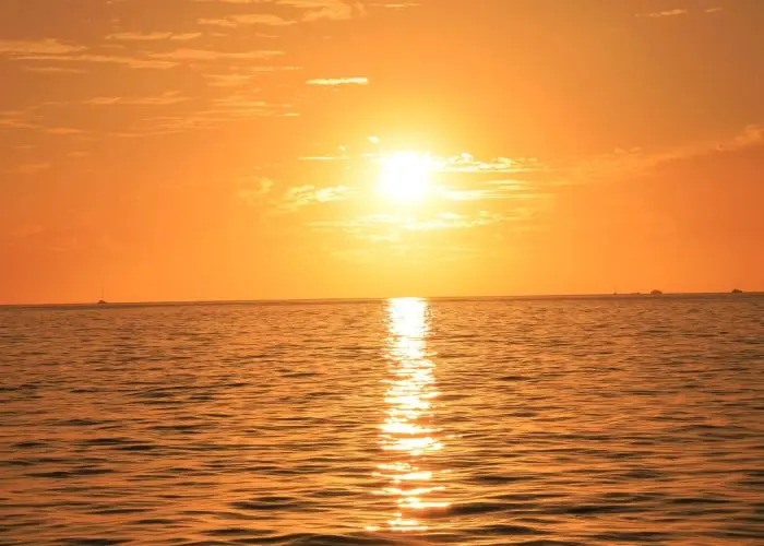 Orange sun sinking toward the horizon off Cabo San Lucas with a golden reflection on the water