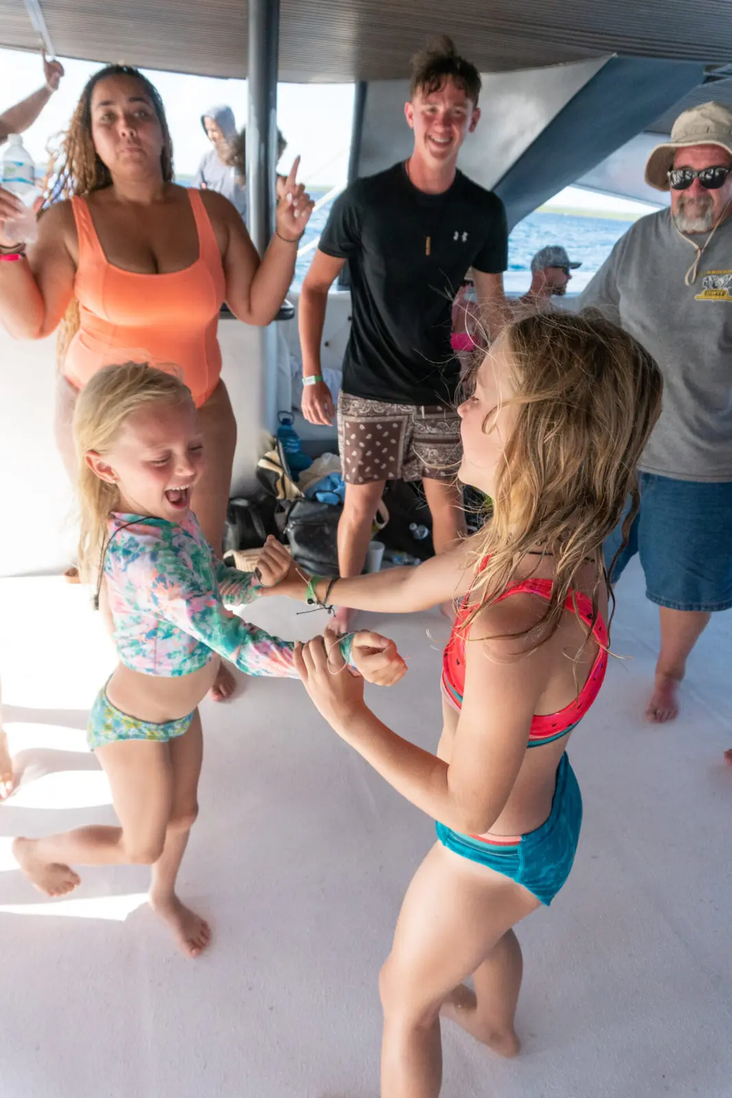 Two girls dancing hand in hand on the catamaran deck as adults look on