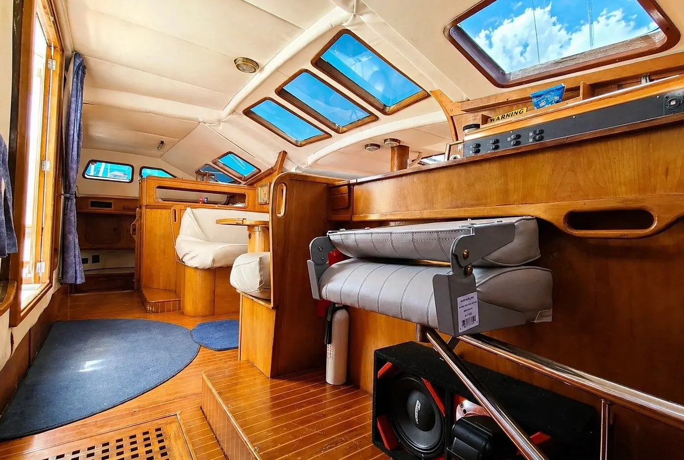 Varnished wood interior below deck with a navigation desk, white cushioned seats and skylight hatches