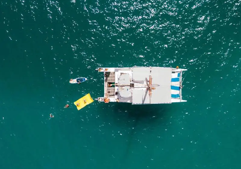 Overhead view of the catamaran anchored in green water off Cabo San Lucas with swimmers and a yellow float