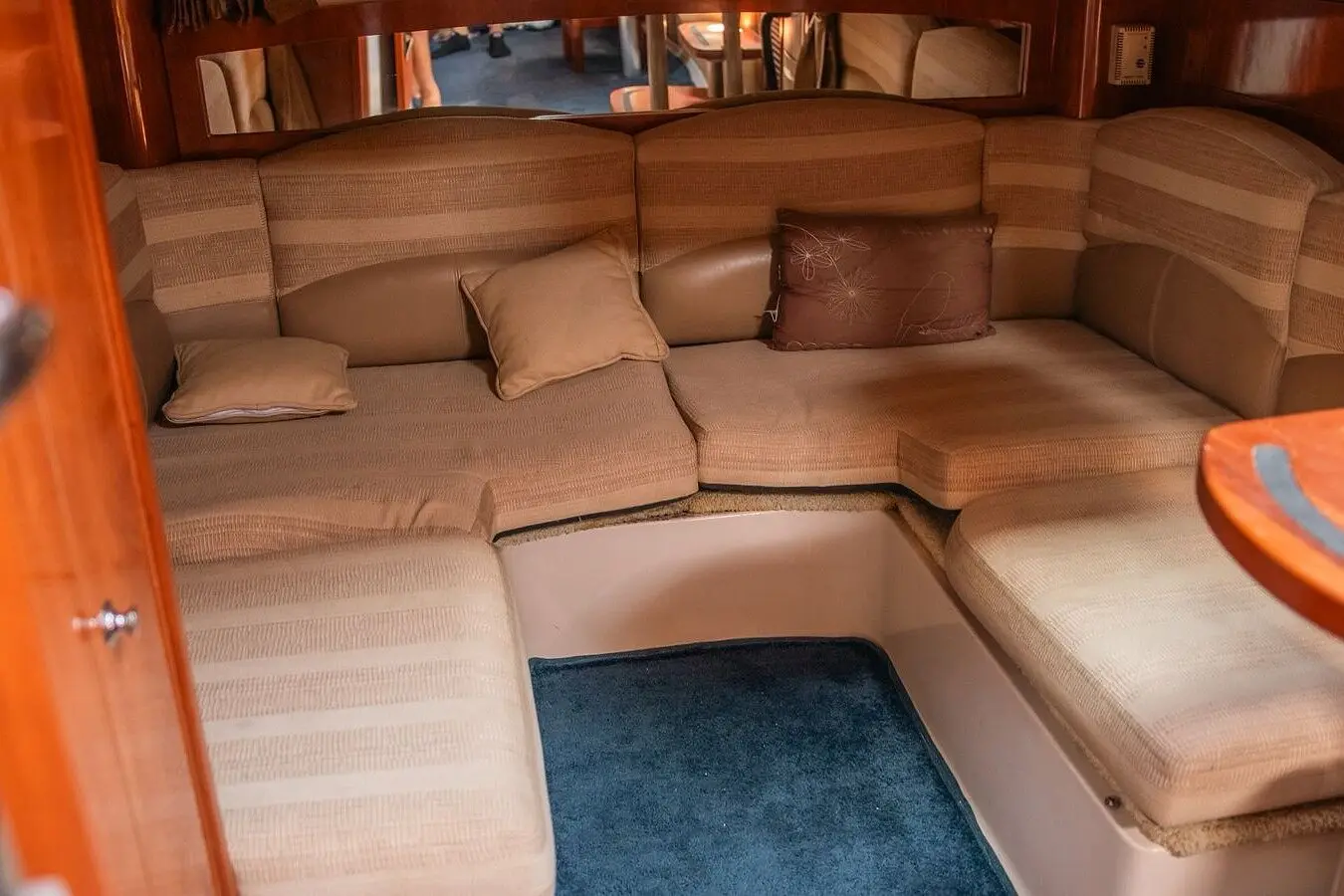 Motor yacht cabin below deck with U-shaped beige cushioned seating, throw pillows and blue carpet