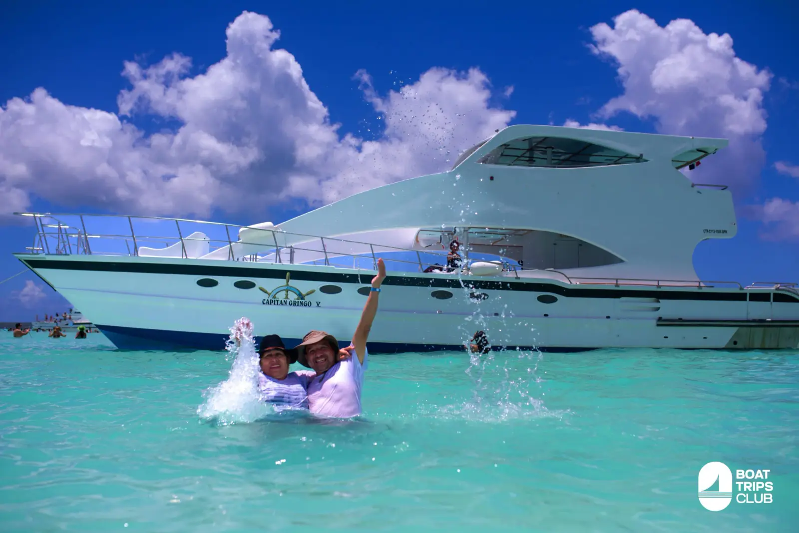 Two guests splashing in turquoise shallows in front of a large white catamaran off Saona Island