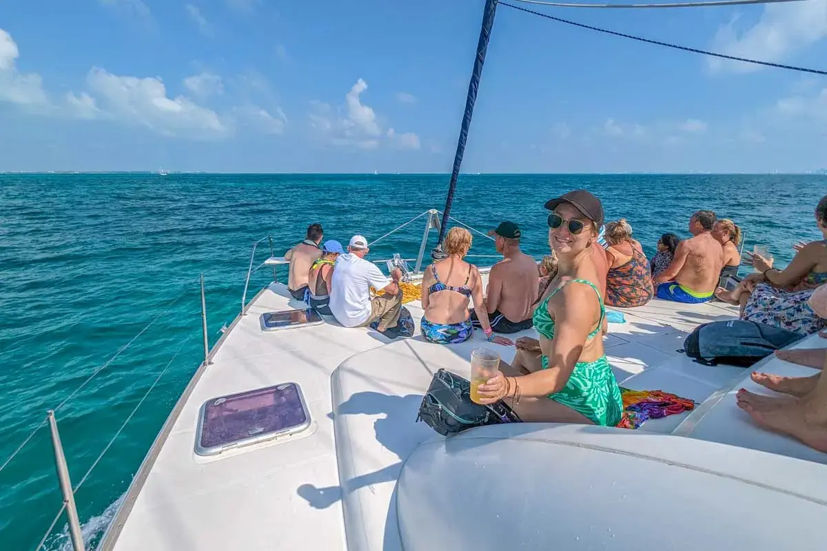 Guests relaxing with drinks on the catamaran's front deck while sailing the open sea off Cancún