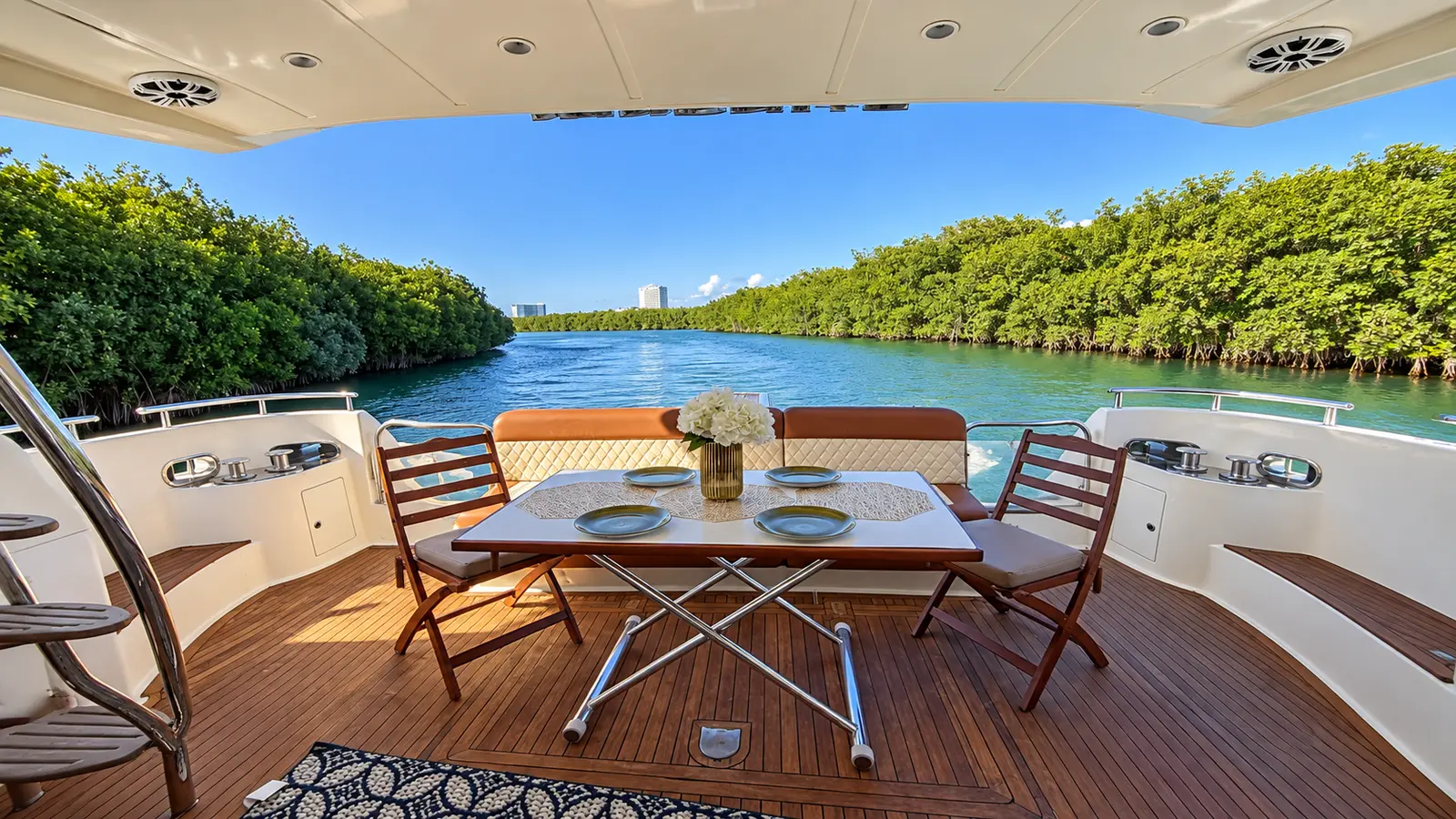 Teak dining table set on a yacht's shaded aft deck, overlooking a mangrove-lined lagoon in Cancún