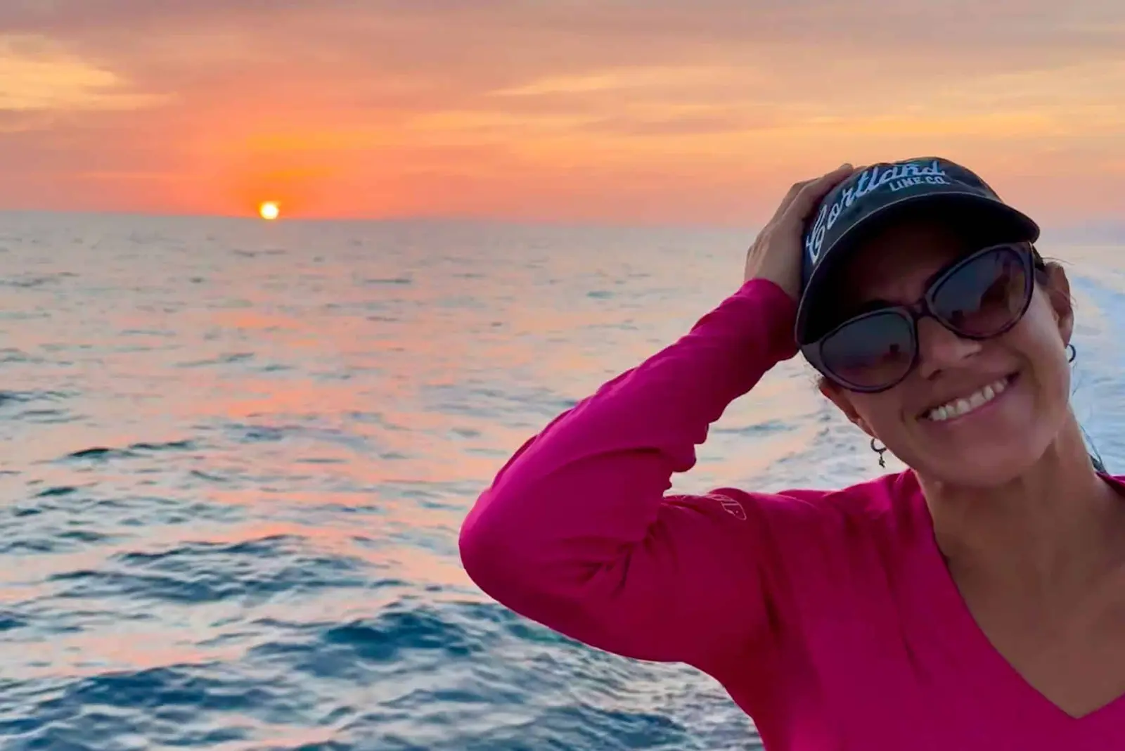 Smiling woman in a pink top and cap aboard as the sun sets over the Pacific off Costa Rica