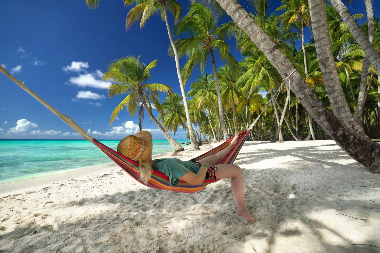 Woman in a sun hat relaxing in a striped hammock between palms on a white-sand beach near Punta Cana