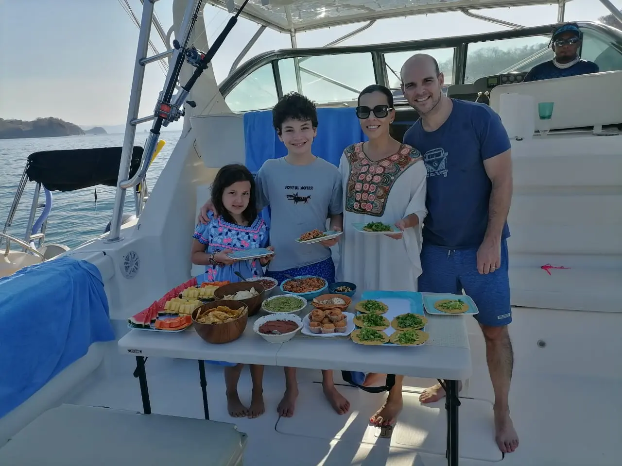 Family with two kids standing behind a table of snacks and dips in the cockpit of a sportfishing yacht