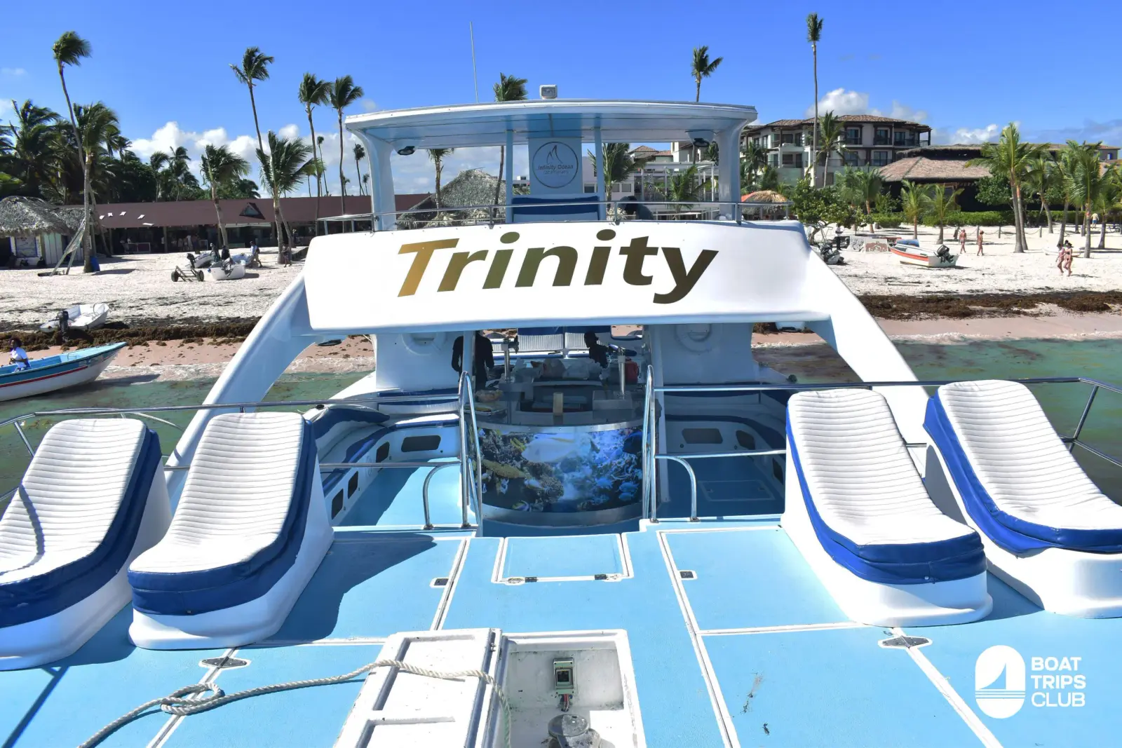 Four blue loungers on a catamaran foredeck below the upper deck, moored off a Punta Cana resort beach
