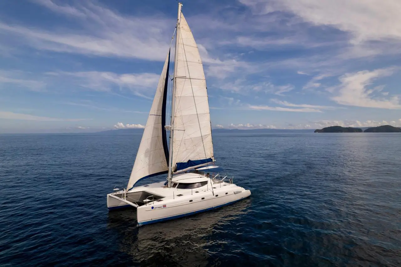 Sailing catamaran under full sail on calm deep blue water with an island on the horizon off Guanacaste