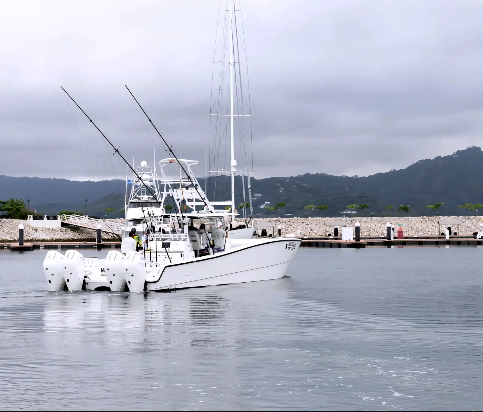 Sportfishing catamaran with a bank of outboards motoring through a calm marina below green hills in Costa Rica