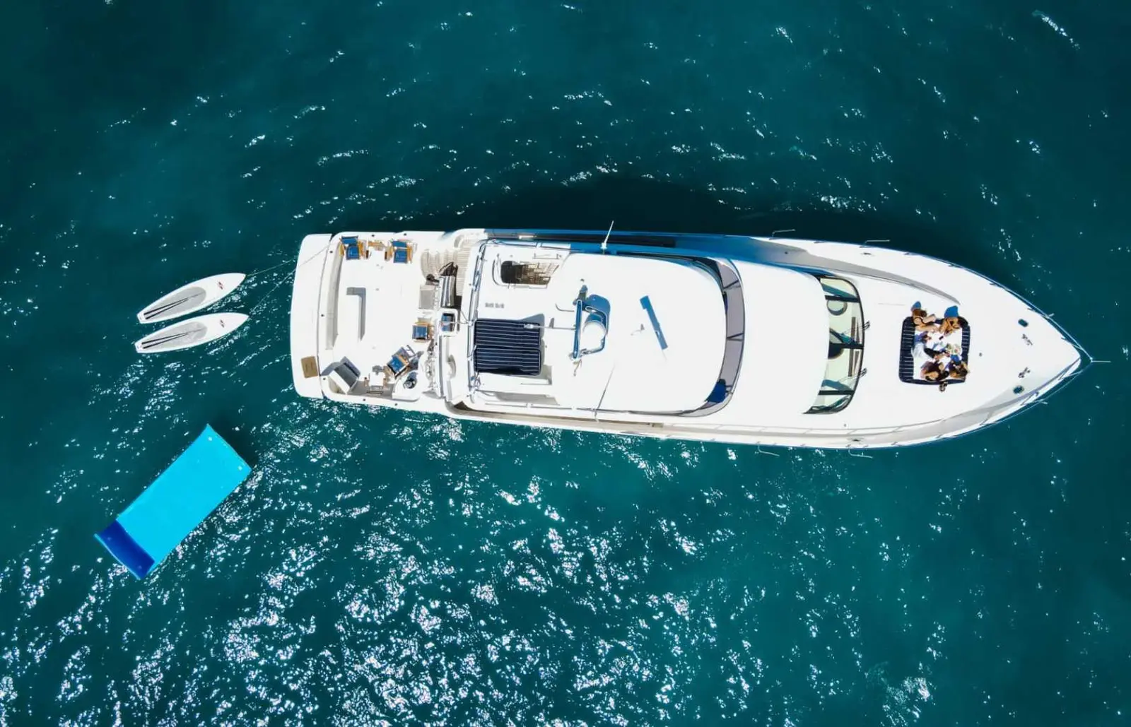 Top-down view of a motor yacht anchored off Cabo San Lucas with paddleboards and a floating mat at its stern