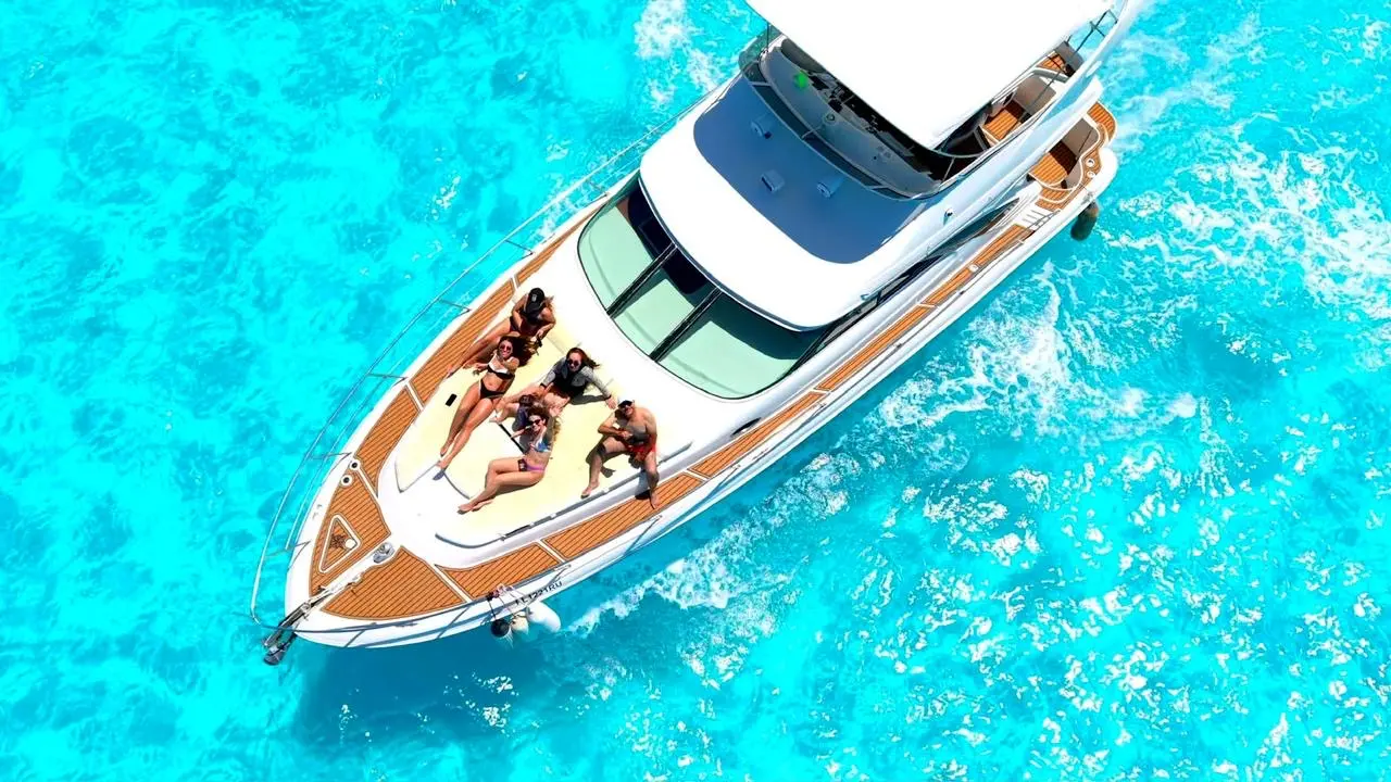 Overhead view of four guests sunbathing on the bow of a motor yacht in turquoise water off Cancún