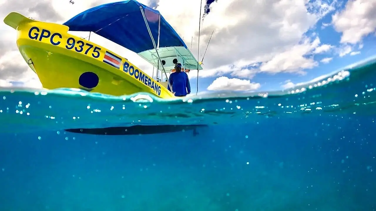 Over-under view of a yellow fishing boat with a blue canopy on clear turquoise water off Playa Flamingo